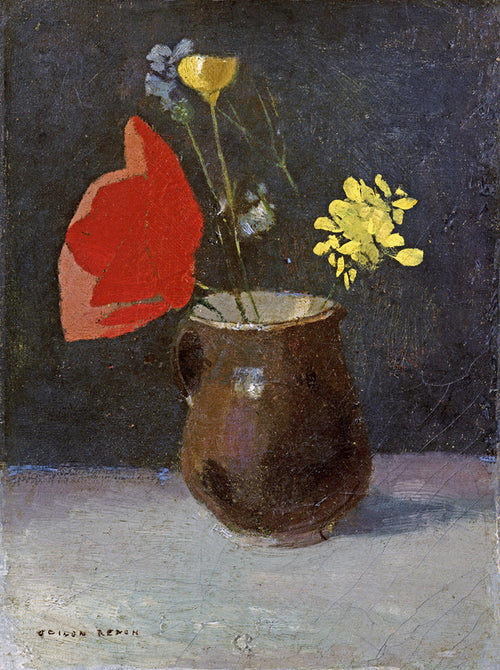 A brown ceramic pitcher containing red, yellow, and blue flowers against a dark background on a light surface.