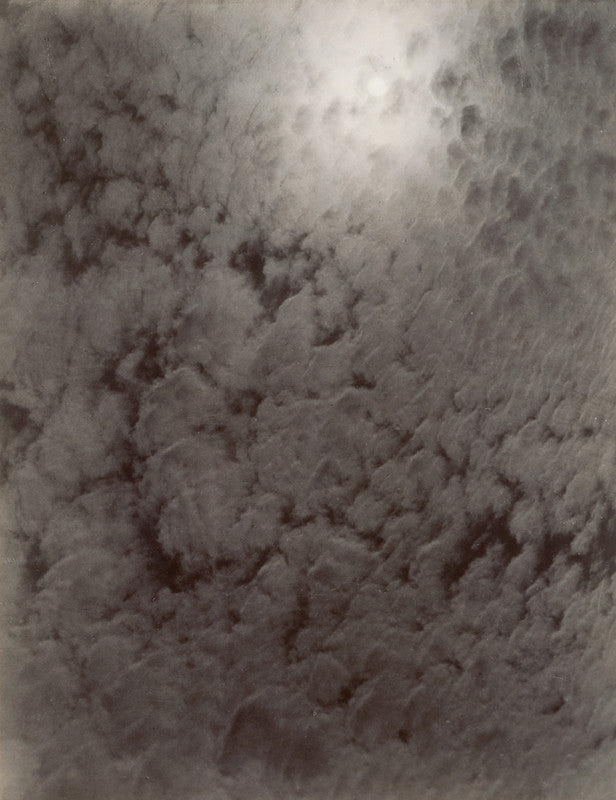 Cloud formation photographed from below, showing white and gray tones with textured cumulus clouds against a lighter sky.