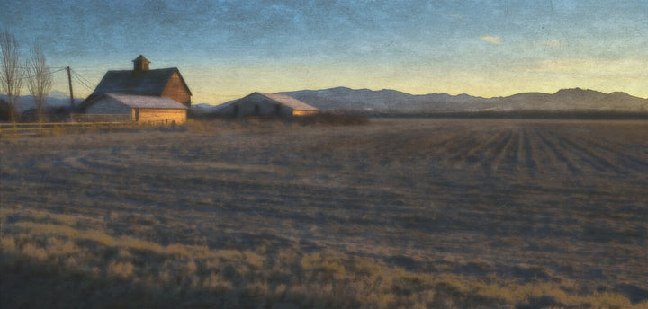 A wooden farmhouse with barn stands in a plowed field beneath mountains at golden hour, rendered in warm and cool tones.