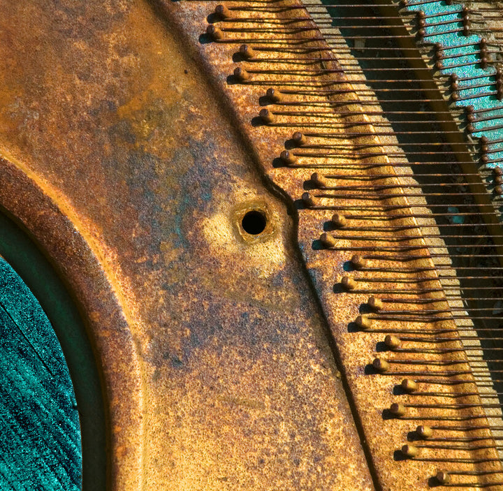 Rusted metal piano keys and machinery detail shot with warm brown and turquoise tones creating strong diagonal shadows.
