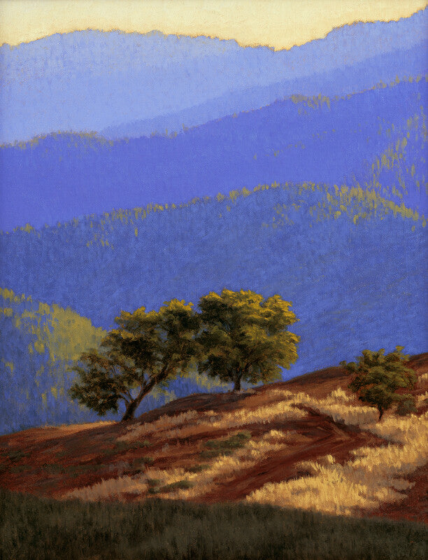 Two trees stand on a reddish-brown hillside with blue mountains and pale sky in the background.