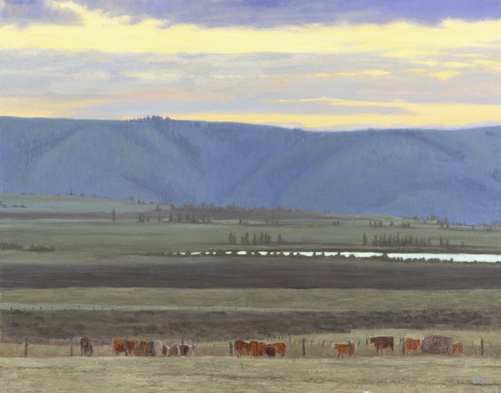 Cattle graze in a pastoral valley landscape with forested mountains under a golden sunset sky.