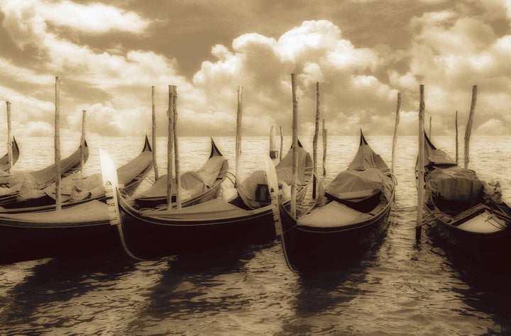 Sepia-toned photograph of multiple gondolas moored in shallow water with wooden poles, cloudy sky beyond.