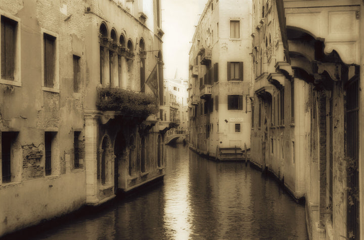 A sepia-toned view of a narrow Venetian canal lined with weathered stone buildings and crossed by small bridges.