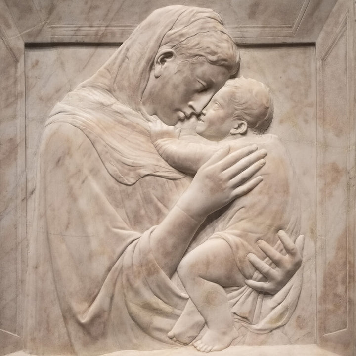 A marble relief sculpture depicts a woman holding and gazing down at an infant, rendered in pale cream tones.